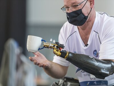 CYBATHLON pilot lifts a tea cup upwards with the help of a prosthetic arm